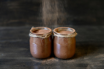 Chocolate mousse in small jars on a wooden background. Cocoa powder on top. Selective focus.