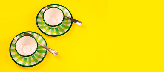 Beautiful little green striped two tea coffee cups and saucers spoons on a yellow background. The concept of home tea drinking, comfort. Banner
