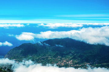 A picturesque mountain landscape with the top of a mountain range above white clouds. On the slope of the mountain there are villages with developed infrastructure. The view from the top. Copy space.