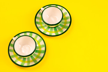 Beautiful little green striped two tea coffee cups and saucers on a yellow background. The concept of home tea drinking, comfort