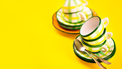 Beautiful little green striped two tea coffee cups stacked one in one and saucers and spoons on a yellow background. The concept of home tea drink