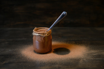 Chocolate mousse in small jars on a wooden background with sprinkled cocoa. Selective focus.Chocolate mousse in a small jar on a wooden background with sprinkled cocoa. Selective focus.