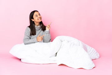 Young mixed race woman wearing pijama sitting on the floor pointing with the index finger a great idea