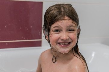Little charming baby girl bathes in a bath with foam