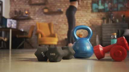 Fitness training at home. Young woman doing leg workout, exercising in living room. Focus on fitness equipment barbell, kettlebell, . Stay at home and stay fit and healthy.