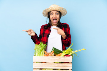 Young farmer Woman holding fresh vegetables in a wooden basket surprised and pointing side