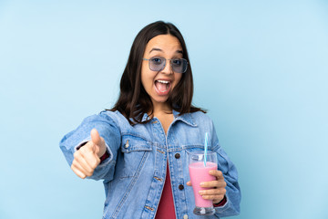 Young woman with strawberry milkshake over isolated blue background with thumbs up because...