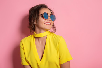 Beautiful girl wearing yellow dress and sunglasses posing on pink background in studio.