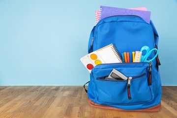 Classic school backpack with colorful school supplies and books on desk.