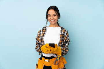 Young electrician woman isolated on blue background sending a message with the mobile