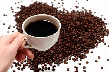 Cup of black coffee in hand close-up. Coffee drink in hand on the background of coffee beans. Coffee beans on the background in the shape of a heart on a blank white background