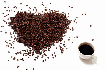 coffee background. Scattered coffee beans on an empty white background in the shape of a heart. Heart of roasted brown coffee beans on a white background along with a Cup of black coffee drink