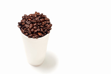 a large cardboard Cup filled with roasted brown coffee beans. the glass is located on a white empty background on the left side of the frame. coffee background for ads, menus or promotions