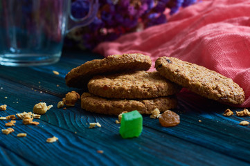 Cereal useful cookies with dried fruit on blue wooden background with pink linen cloth and glasses. Homemade pastries and sweets.