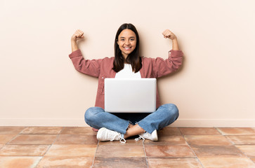 Young mixed race woman with a laptop sitting on the floor doing strong gesture