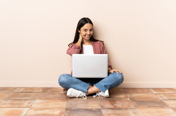 Young mixed race woman with a laptop sitting on the floor laughing