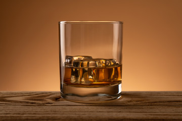 Glasss of whiskey with ice cubes on wooden table