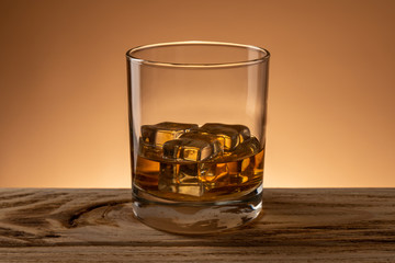 Glass of scotch whiskey with natural ice on wooden table in bar
