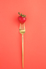 One strawberry on a gold fork in the center of the red  background. Top view. Location vertical. Diet minimal concept.