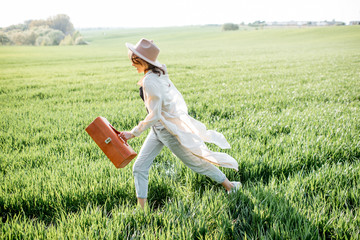 Portrait of a stylish and active woman running with handbag on the greenfield, enjoying nature in springtime. Concept of wellness and carefree lifestyle on nature