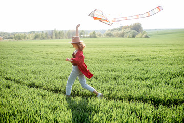 Young carefree woman launching kite on the greenfield. Concept of enjoying nature and active...