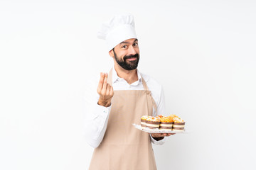 Young man holding muffin cake over isolated white background making money gesture