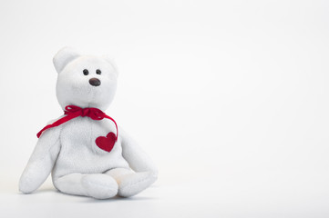 A toy bear is sitting. Red heart and ribbon