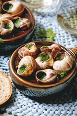 Obraz premium Escargots de Bourgogne - Snails with herbs butter, gourmet dish, in traditional ceramic pan with coriander, bread, glass of white wine on blue straw napkin. Close up