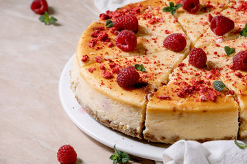 Homemade raspberry baked cheesecake sliced on plate decorated by fresh raspberries and mint over pink marble background with white cloth. Close up