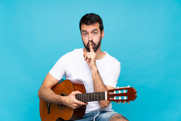 Young man with guitar over isolated blue background showing a sign of silence gesture putting finger in mouth