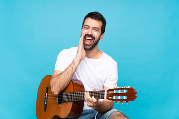 Young man with guitar over isolated blue background shouting and announcing something