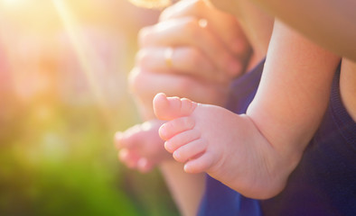 Foot barefoot toddler closeup. Toddler is sitting at his father's neck on the background of soft sunlight and blurred green bokeh. Concept father's day, family day. Family walks in the park.