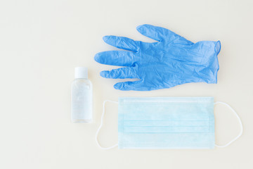 top view of protective stuff, blue medical mask and glove, white bottle of sanitizer on light...