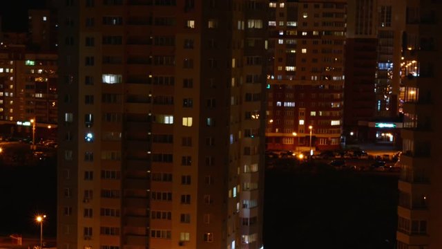 highrise multi-story residential buildings with cars on parking lots and illuminated windows at night zoom in timelapse