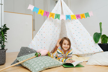 10 years old girl reading in front of a hut with stay home flag garland across