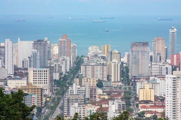 Visão aérea de um trecho da cidade de Santos, São Paulo. Com destaque para a avenida entre os prédios em direção ao mar, que está com alguns navios.