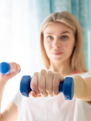 Focus on dumbbells. Woman exercising with dumbbells at home. Blured face