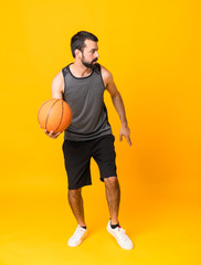 Full-length shot of man over isolated yellow background playing basketball