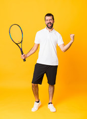 Full-length shot of man over isolated yellow background playing tennis and celebrating a victory