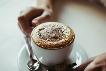 Coffee cappuccino with foam. Women's hands with cap