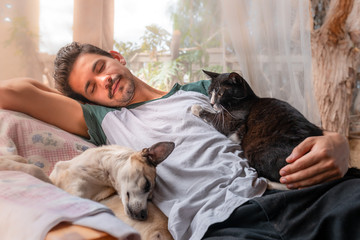 hombre joven duerme junto a un perro y un gato negro en un sillon  bajo una mosquitera. 