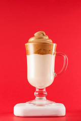 Dalgona coffee in a transparent glass on a red background. Close-up, copy space