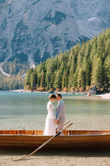 Bride and groom in a wooden boat at the Lago di Braies in Italy. Wedding couple in Europe, on Braies lake, in the Dolomites. The newlyweds are standing in the boat and hugging.