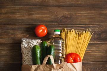 Food supplies. Paper bag with food, stock of non-perishable products and vegetables on a wooden background. Beans, sunflower oil, pasta. Food Delivery, Donation, Coronavirus Quarantine. Copyspace.