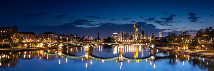 Fototapeta na wymiar Illuminated Cityscape of Frankfurt am Main, Germany at Night with Reflective Bridge