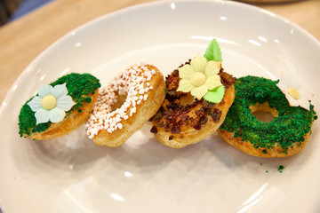 four round profiteroles cakes with colorful sprinkles on a white dish