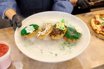 four round profiteroles cakes with colorful sprinkles on a white dish