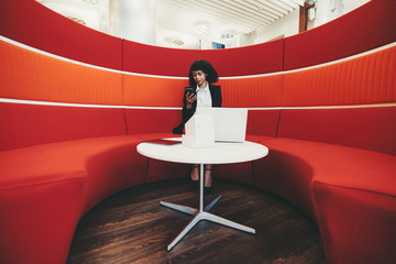 Wide-angle shot of a young charming African-American businesswoman sitting on a curved sofa of red...
