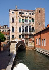 Fototapeta na wymiar Photo of canal in Venice with historical facades with balustrades, greenery, lantern and bridge.