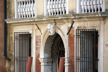 Photo of entrance in Venice with female head, balustrade and pilasters made in baroque style.